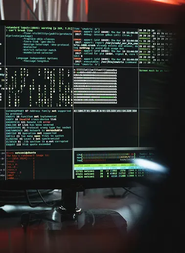 Multi-monitor setup with glowing code editors, terminals, and system dashboards on dark screens.