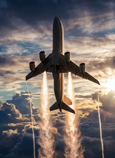 Rear view of a large commercial jet flying away, engine pods visible, silhouetted against a sunset sky with contrails and clouds.