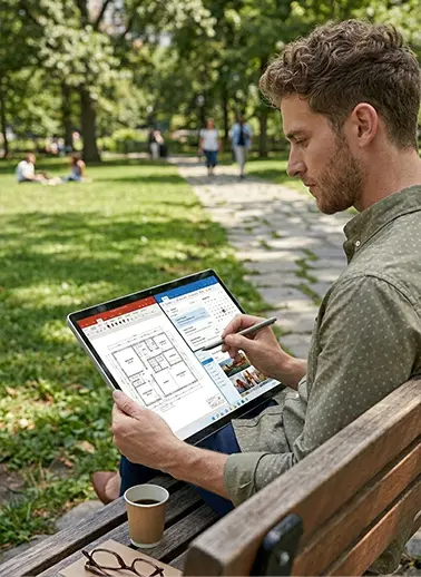 Man on a park bench uses a tablet to view architectural floor plans, with a coffee cup and glasses nearby in a sunny park setting.